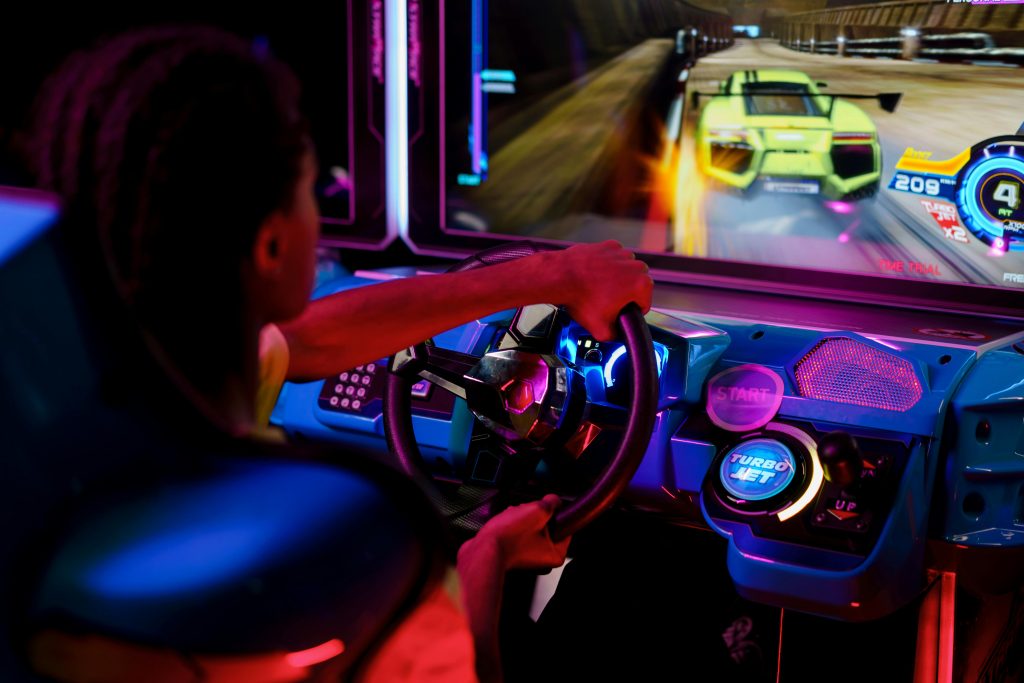 A person playing an immersive arcade racing game with vibrant lights.